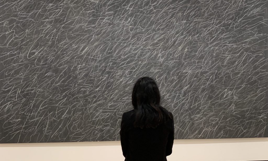 Rebecca Mangra looking at a piece of artwork that features white scribbles on a chalkboard.