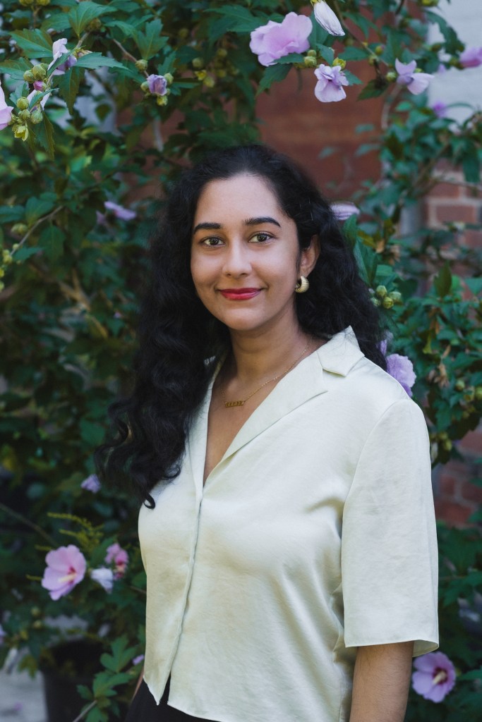 Headshot of Rebecca Mangra in front of purple flowers.